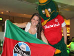 Momento Gre-Nal: torcedora mostra bandeira com simbolo tricolor, enquanto outro torcedor, caracterizado, veste camisa colorada.