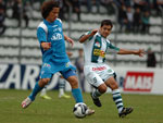 Odair tocando a bola enquanto Lauro chega para marcar