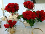 Bules, taas e at aucareiros de prata fazem as vezes de vaso para as rosas vermelhas. Esta proposta  de uma mesa mais sofisticada